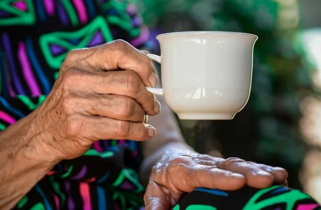 Mains d’une personne âgée tenant une tasse de thé blanche
