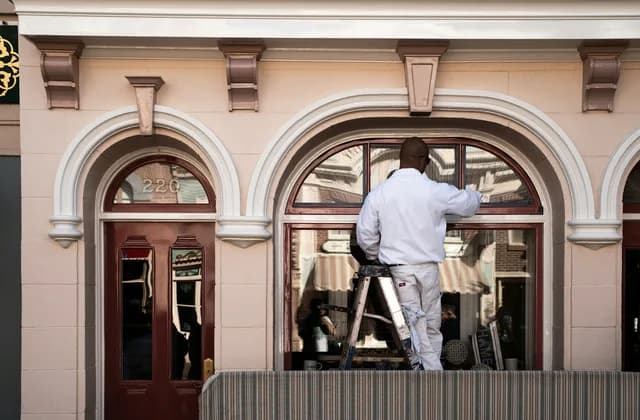 Artisan sur un escabeau devant une fenêtre cintrée de façade