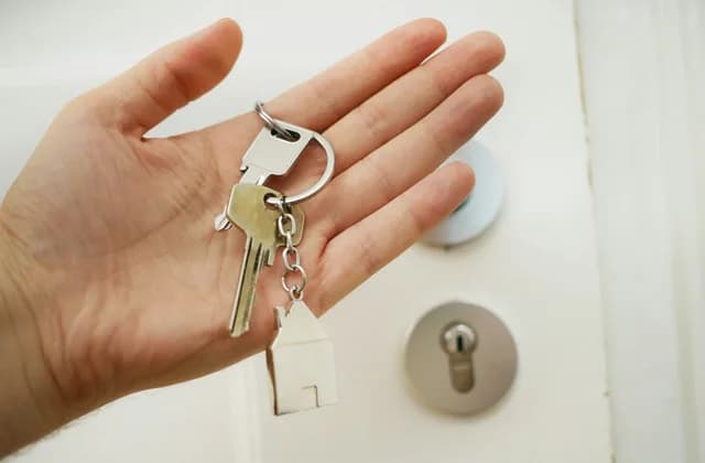 Mão segurando chaves diante de uma porta com fechadura