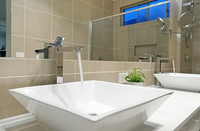 Baño con muros de azulejo beige, lavabo blanco y regadera de vidrio