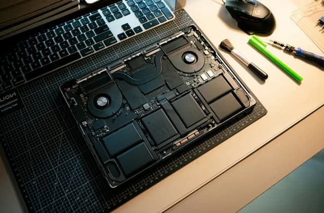 Open laptop showing its internal components on a desk next to repair tools