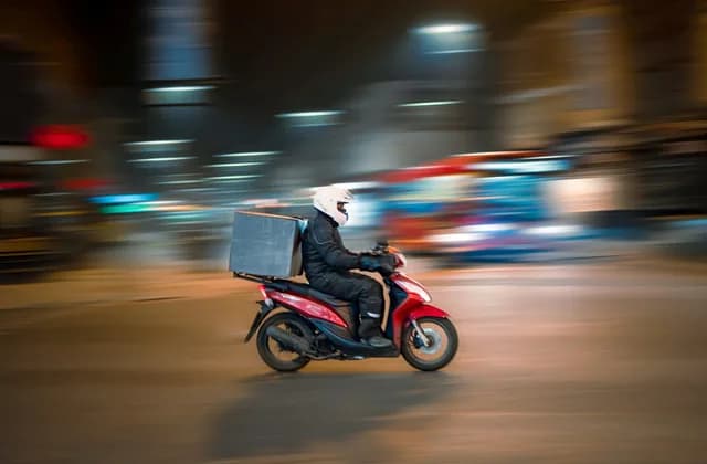 A delivery rider with a top box riding through a city at night