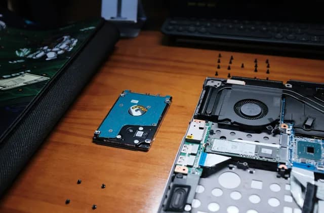 Ordinateur portable ouvert et disque dur posés sur un bureau en bois pendant une réparation