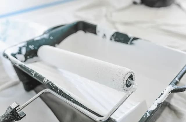 Paint roller resting in a white paint tray on a dust sheet
