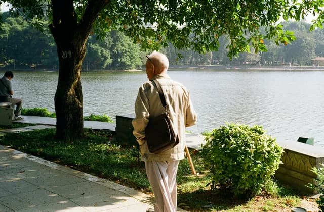 Older man with a shoulder bag walking along a lakeside path, seen from behind