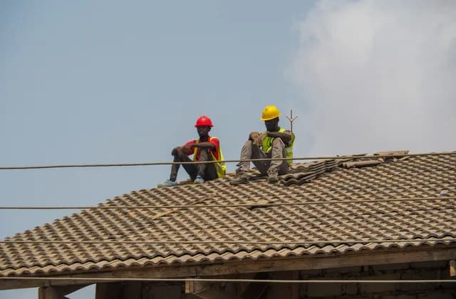 Dos trabajadores con casco sentados sobre un techo de teja