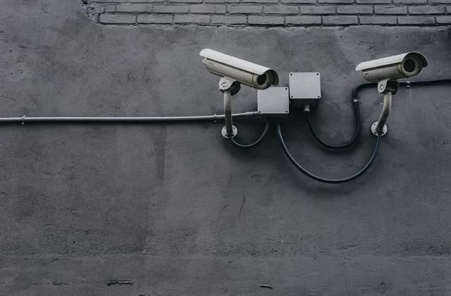 Dos cámaras de seguridad montadas en un muro gris con su cableado