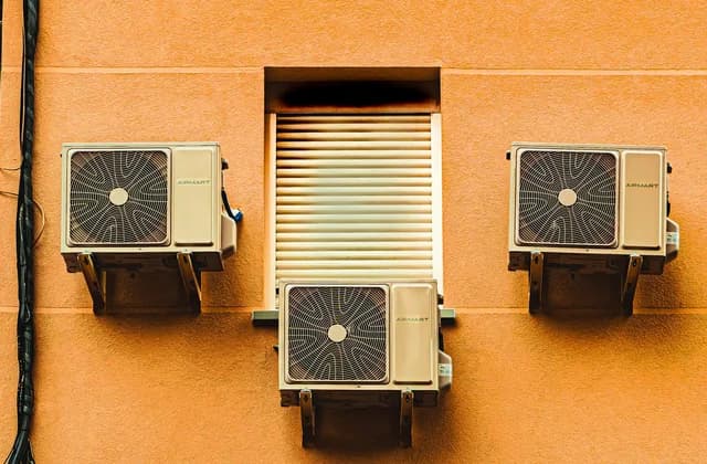Tres condensadoras de minisplit en una pared naranja junto a una ventana
