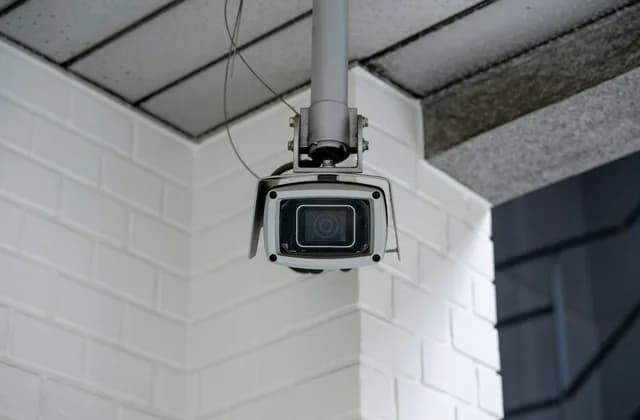Caméra de surveillance fixée sous un auvent, contre un mur de briques blanches