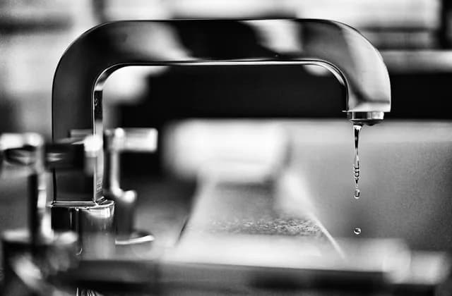 Tropfender Wasserhahn über einem Waschbecken in Schwarz-Weiß