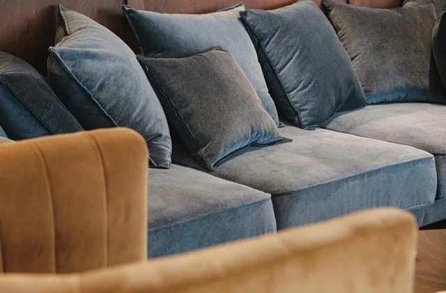 Sala de terciopelo gris azulado con cojines y un sillón color mostaza en primer plano