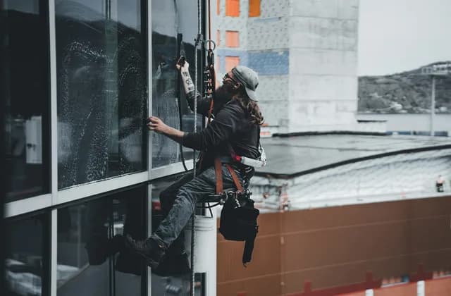 Profissional com equipamento de segurança limpando a fachada de vidro de um prédio