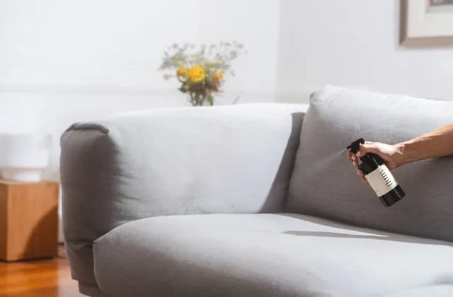 Main vaporisant un produit textile sur un canapé en tissu gris