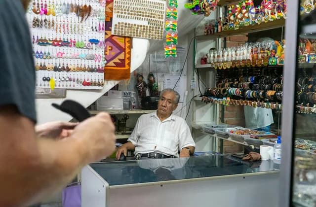 Dueño de una tienda de artesanías y bisutería detrás del mostrador, frente a un cliente