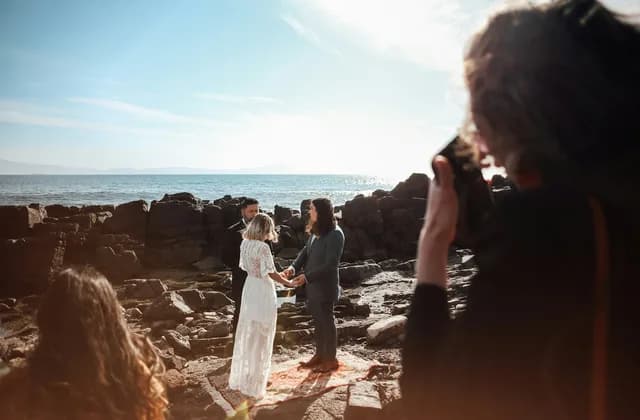 Photographe de dos face à des mariés au bord de la mer
