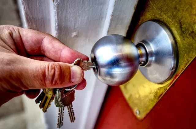 Una mano introduce la llave en el pomo cromado de la puerta de entrada de una vivienda