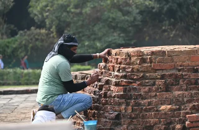 Un operario coloca ladrillos a mano sobre un muro, arrodillado junto a la hilada