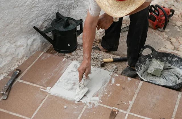 Manos rellenando con mortero las juntas de un suelo de baldosas de barro junto a las herramientas