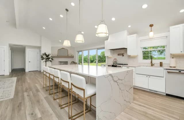 Cocina blanca con isla de piedra veteada tipo mármol y taburetes