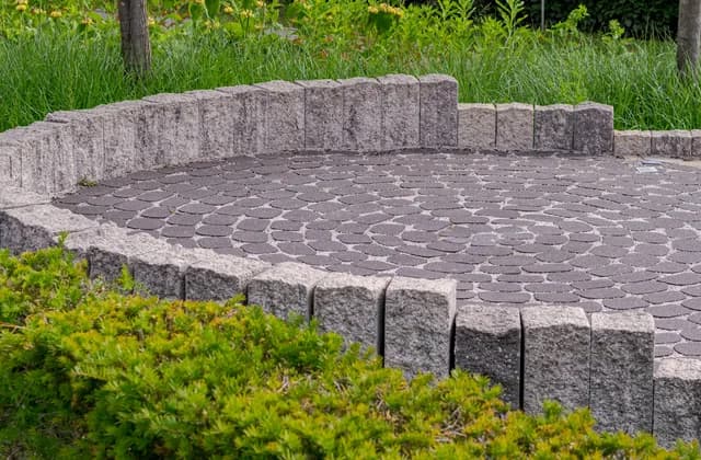 Zona redonda pavimentada con adoquines y rodeada de bordillos de granito en un jardín