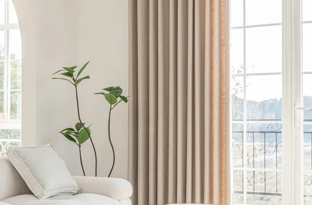 Cortina de lino beige hasta el suelo junto a una puerta balconera con barandilla de hierro