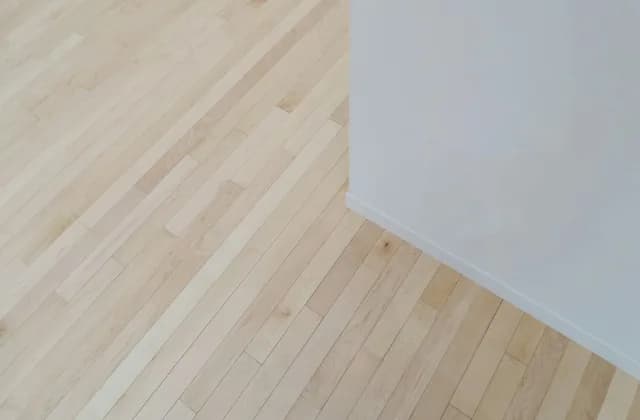 Piso de madera clara en una habitación vacía junto a una pared blanca