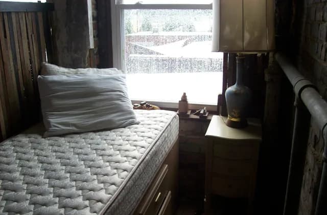 Matelas nu et oreiller sur un lit près d’une fenêtre, dans une chambre