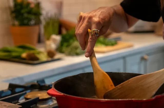 A cook stirring a pot with a wooden spoon on a home kitchen stove