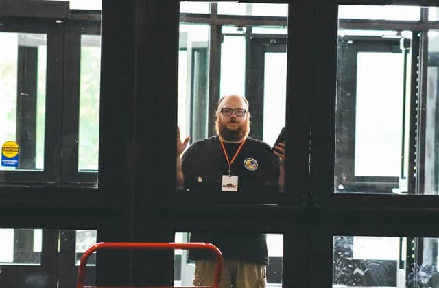 A uniformed security guard at the glass entrance of a building