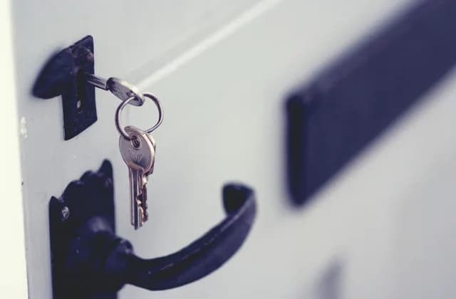 Clés insérées dans la serrure d’une porte blanche à poignée noire