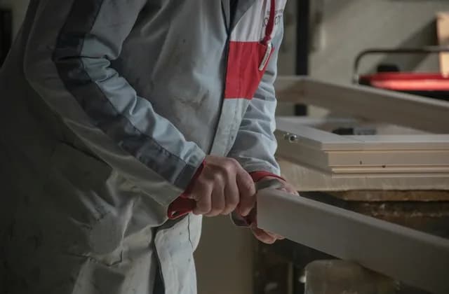 Artisan en tenue de travail tenant une pièce de bois dans son atelier