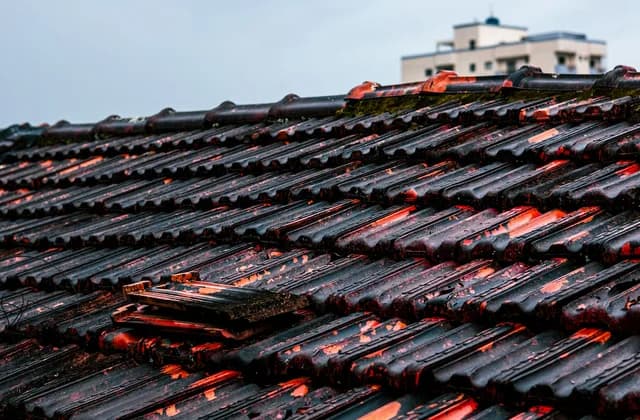 Yağmurla ıslanmış eski bir kiremit çatıda kırılıp yerinden kaymış kiremitler; arka planda bir apartman