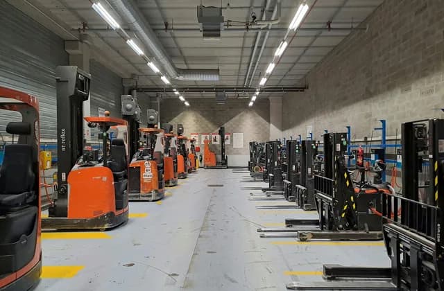 Reihe von Schubmaststaplern und Elektro-Hubwagen in einer Lagerhalle, davor markierte Stellplätze