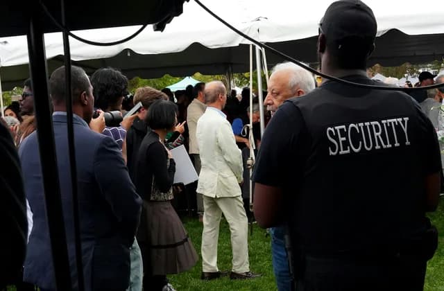 Sicherheitsmitarbeiter mit SECURITY-Aufdruck am Rücken beobachtet eine Menschenmenge bei einer Veranstaltung im Freien