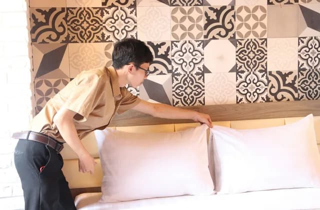 Person im Hoteldienst richtet die Kopfpolster auf einem frisch bezogenen Bett her