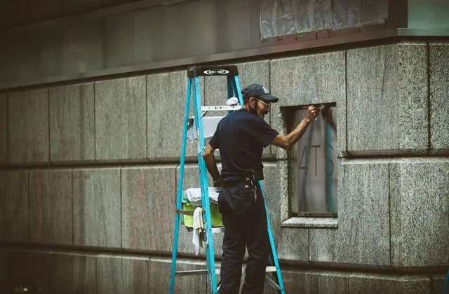 Trabajador en una escalera instalando una ventana en una fachada