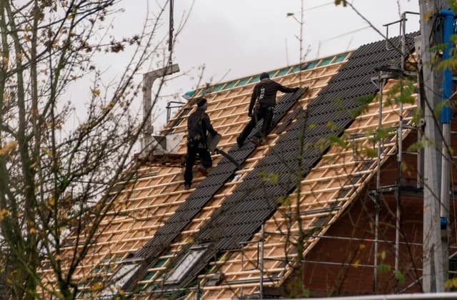 Dachdecker auf einem Gerüst decken ein steiles Dach neu ein