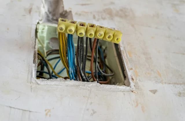 Duvardaki açık buatta klemenslerle bağlanmış renkli elektrik kabloları