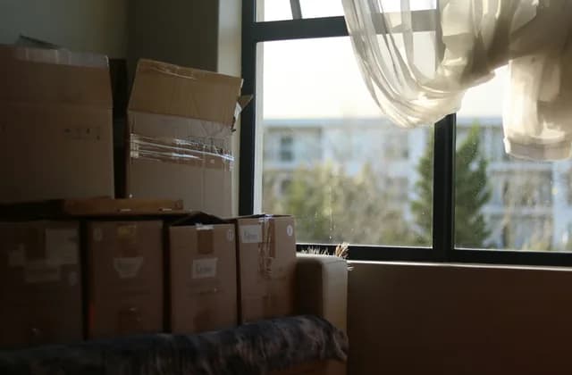 Taşınma öncesi kolilerle dolu bir oda; pencereden karşıdaki apartman blokları görünüyor