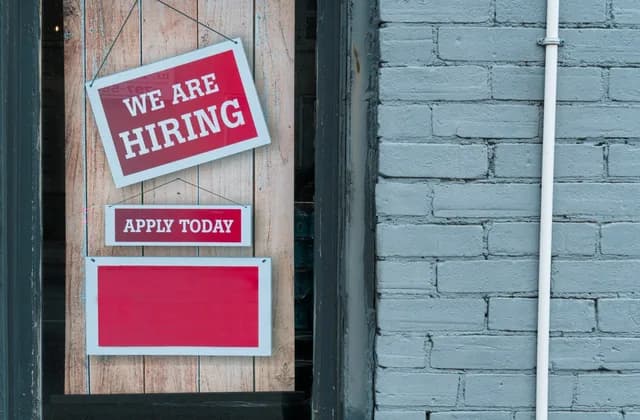 A “We are hiring – Apply today” sign hanging in a shop window