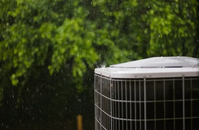 Central air conditioner condenser outside a house in the rain