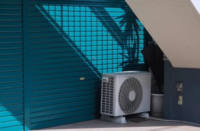 Unité extérieure de climatisation au pied d’un mur bleu