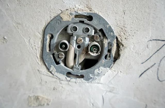 Sıvalı bir duvarda kapağı sökülmüş, iç mekanizması ve bağlantı vidaları görünen topraklı priz