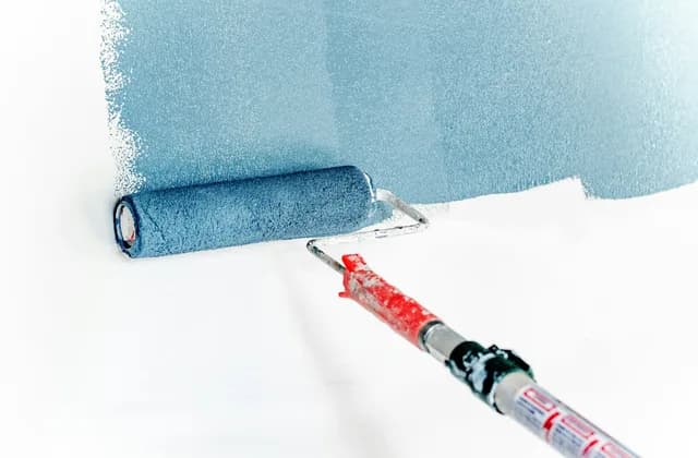 Eine Farbrolle trägt blaue Wandfarbe auf eine weiße Wand auf