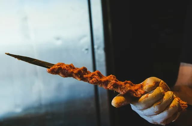 Eldivenli bir elde, şişe sarılmış baharatlı kıyma kebabı