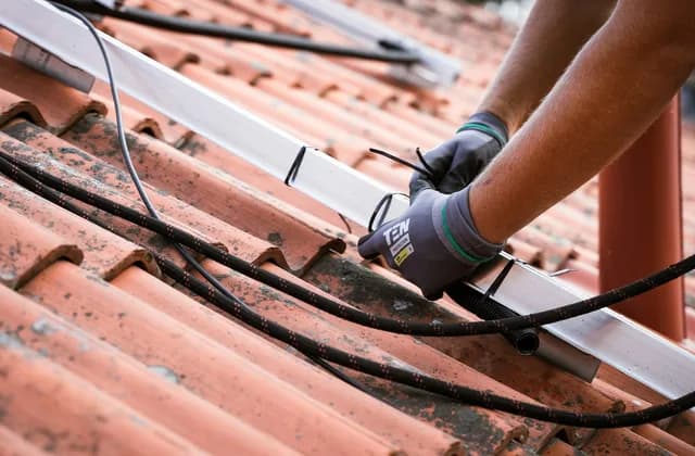 Mãos com luvas trabalhando sobre telhas cerâmicas de um telhado